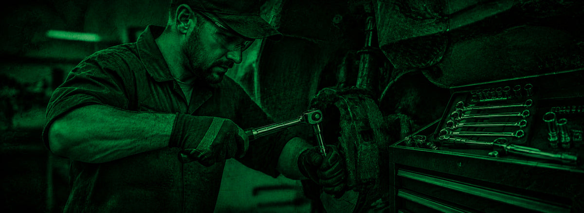 Mechanic wearing gloves repairs a vehicle engine beside an open tool chest in a dim workshop